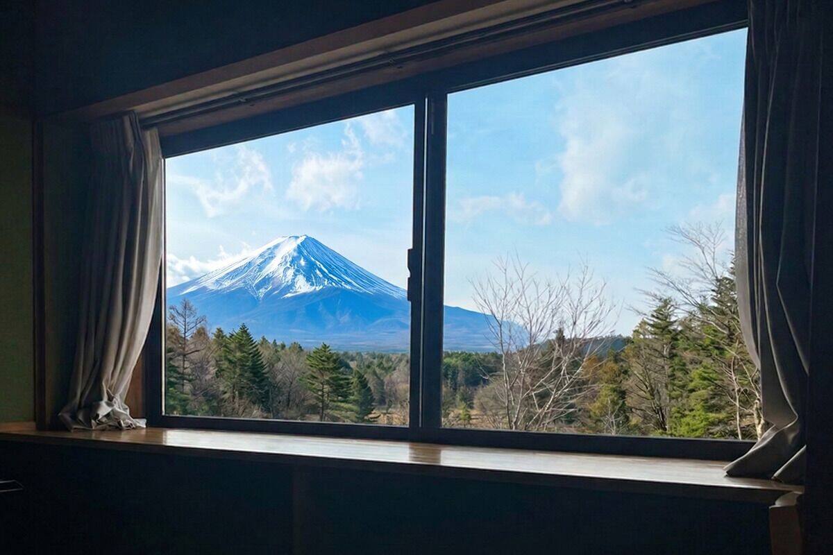 Ein Fenster mit Blick auf einen schneebedeckten Berg und eine bewaldete Landschaft.