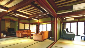 Une pièce de style japonais traditionnel, avec un sol recouvert de tatamis, un canapé, un fauteuil et un téléviseur.