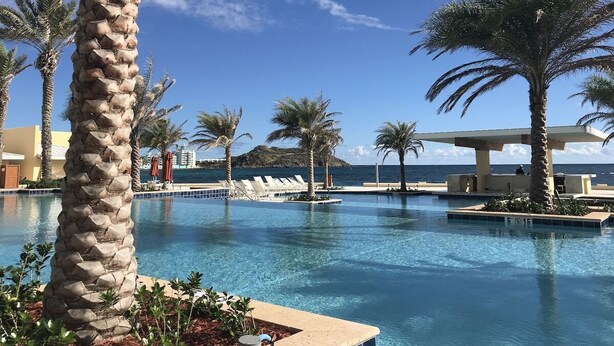 Un área de piscina con palmeras, sillas de descanso y vistas al océano.