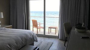 Habitación de hotel con cama, escritorio, silla y vista al océano a través de un amplio ventanal corredero.