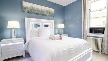A bedroom with a large bed, two bedside tables with lamps, a radiator, and a window with curtains.