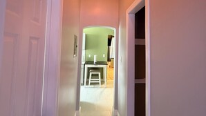 Un pasillo con una lámpara en el techo, una puerta y vista a una habitación con radiador.