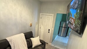 Una sala de estar moderna con un sofá de cuero, un televisor de pantalla plana montado en la pared y un pasillo que conduce a una puerta.