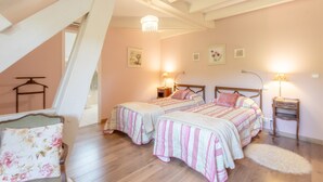 Une chambre avec deux lits, un plancher en bois, un lustre et des lampes de chevet.