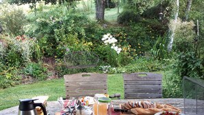 Une table de jardin dressée pour un repas en plein air, avec de la nourriture et des boissons, le tout entouré de verdure.