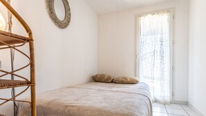 A bedroom with a bed, a wicker chair, a mirror, and a window with curtains. - Domaine Grand Plage by Interhome (Cap d'Agde)