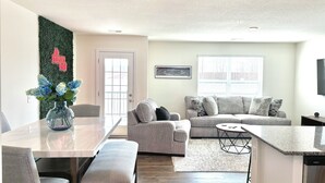 A modern living room with a grey sofa, a dining table with chairs, and a kitchen area with a built-in dishwasher. - Raceday Getaway, 3BR/2.5BA home right across from Bristol Motor Speedway! (Bristol)