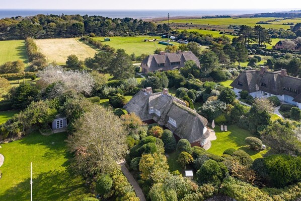 Una finca rural con casas de techo de paja, extensos campos verdes y un pequeño jardín.