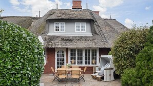 A thatched-roof house with a stone patio, a wooden table, and outdoor seating. - Haus Kamp - Exclusive thatched house for 6 pers. with sauna, fireplace, garden, car (Kampen (Sylt))