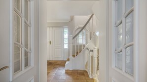 A hallway with white doors, a wooden floor, and a staircase with white railings. - Haus Kamp - Exclusive thatched house for 6 pers. with sauna, fireplace, garden, car (Kampen (Sylt))