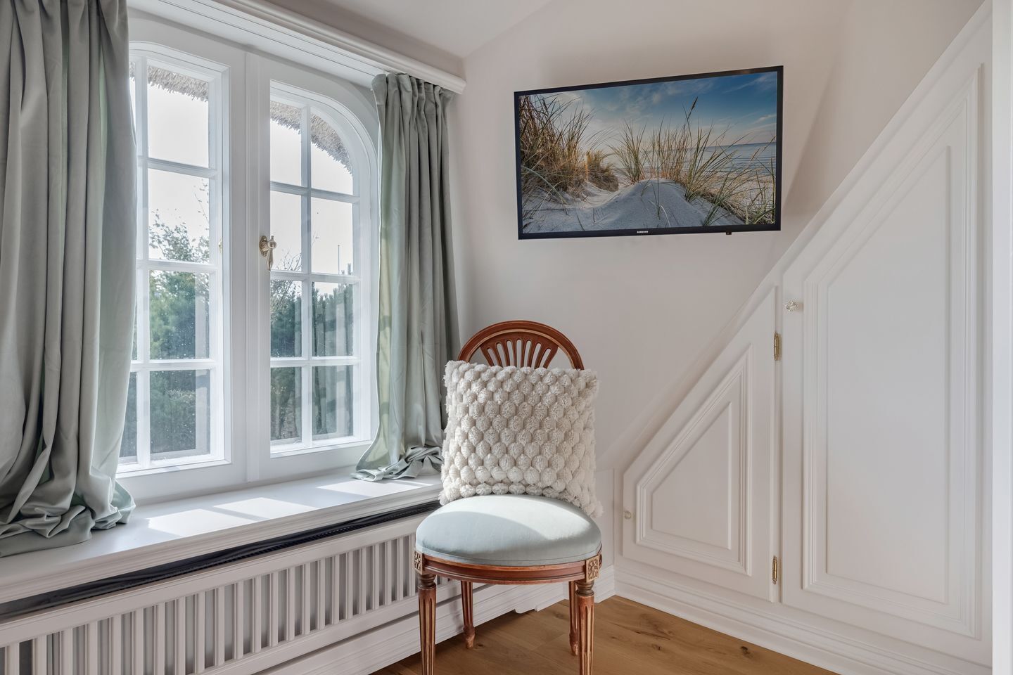 Um quarto com janela, radiador, uma cadeira e um quadro na parede.