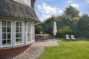 A house with a thatched roof, a stone patio with outdoor furniture, and a well-maintained lawn. - Haus Kliff - Exclusive 5 star thatched house for 5 pers. with sauna, garden, car (Kampen (Sylt))