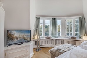 A bedroom with a large window, a bed, a TV, and a radiator. - Haus Kliff - Exclusive 5 star thatched house for 5 pers. with sauna, garden, car (Kampen (Sylt))