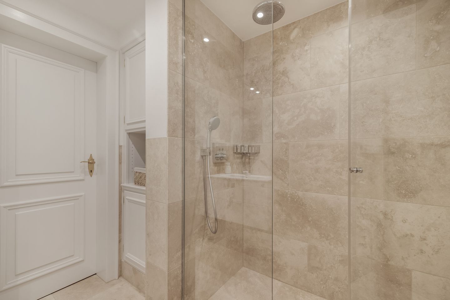 A modern bathroom with a glass-enclosed shower, white cabinetry, and beige tiles.