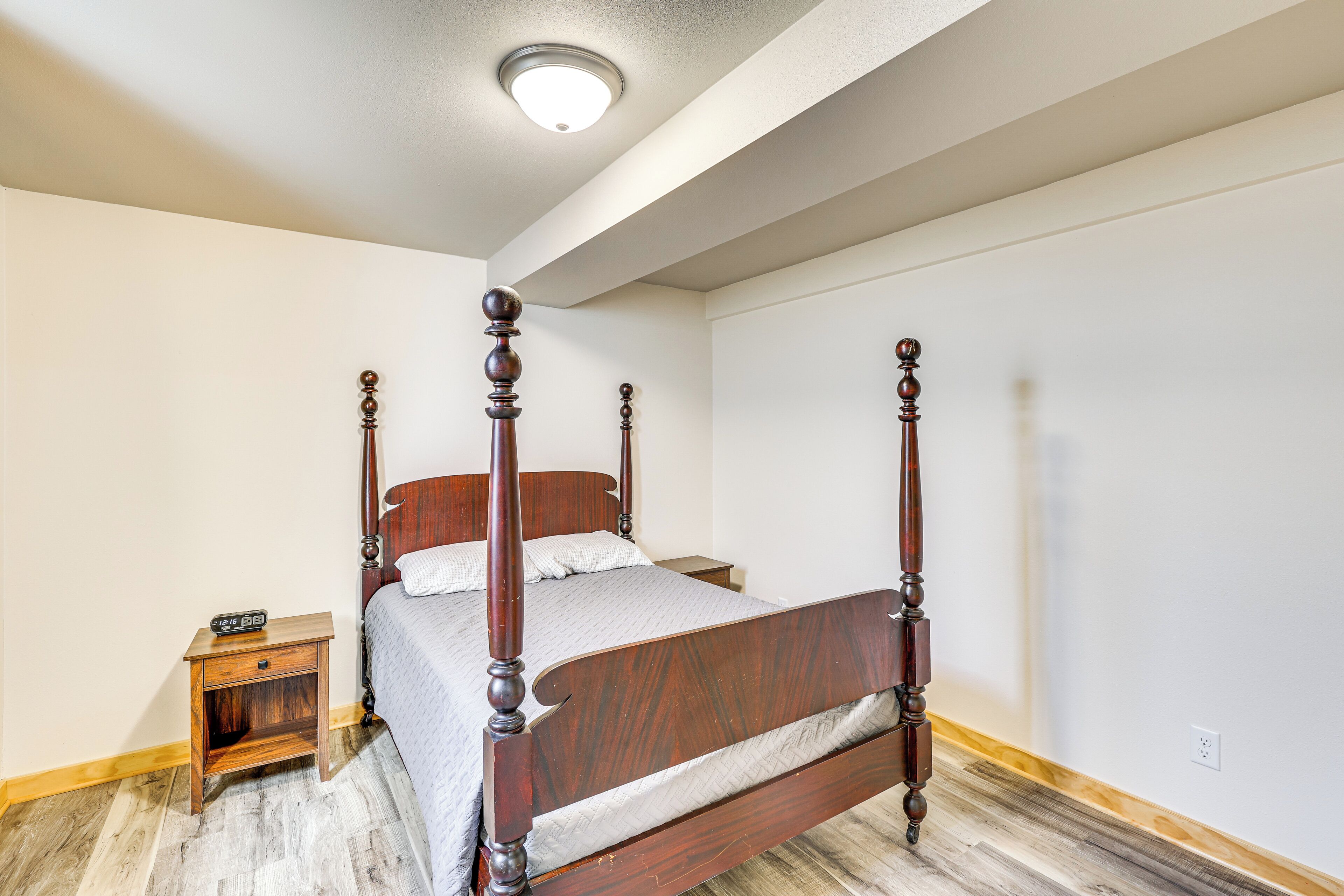 A four-poster bed in a bedroom with a nightstand, a ceiling light, and a wooden floor.