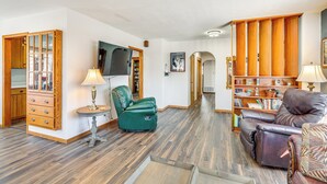 Een ruime woonkamer met een houten vloer, een groene leren fauteuil, een bruine leren bank, een houten kast en een boekenplank.