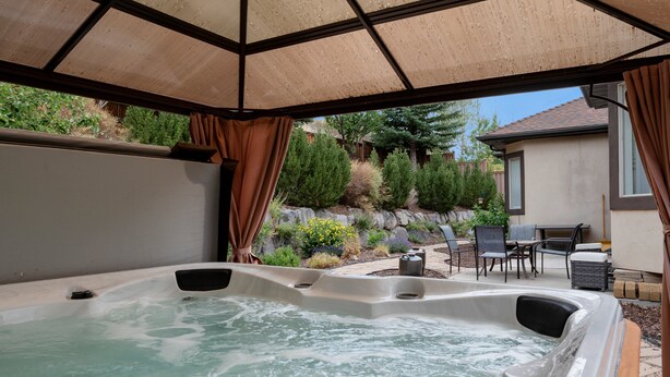 Un espace avec un jacuzzi, surmonté d’une pergola, entouré d’un jardin aménagé et de mobilier de patio.