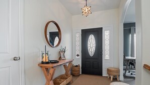 Un couloir avec une console en bois, des paniers en osier, un miroir rond et une porte noire dotée d’une vitre.
