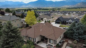 Un quartier résidentiel avec des maisons, un grand arbre et des montagnes en arrière-plan.