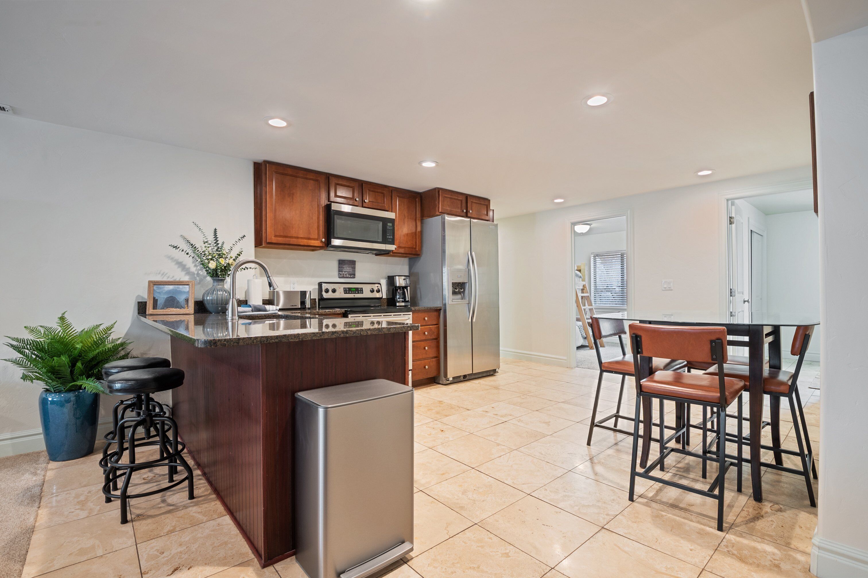 A modern kitchen with wooden cabinets, stainless steel appliances, a bar stool, and a dining area with chairs.