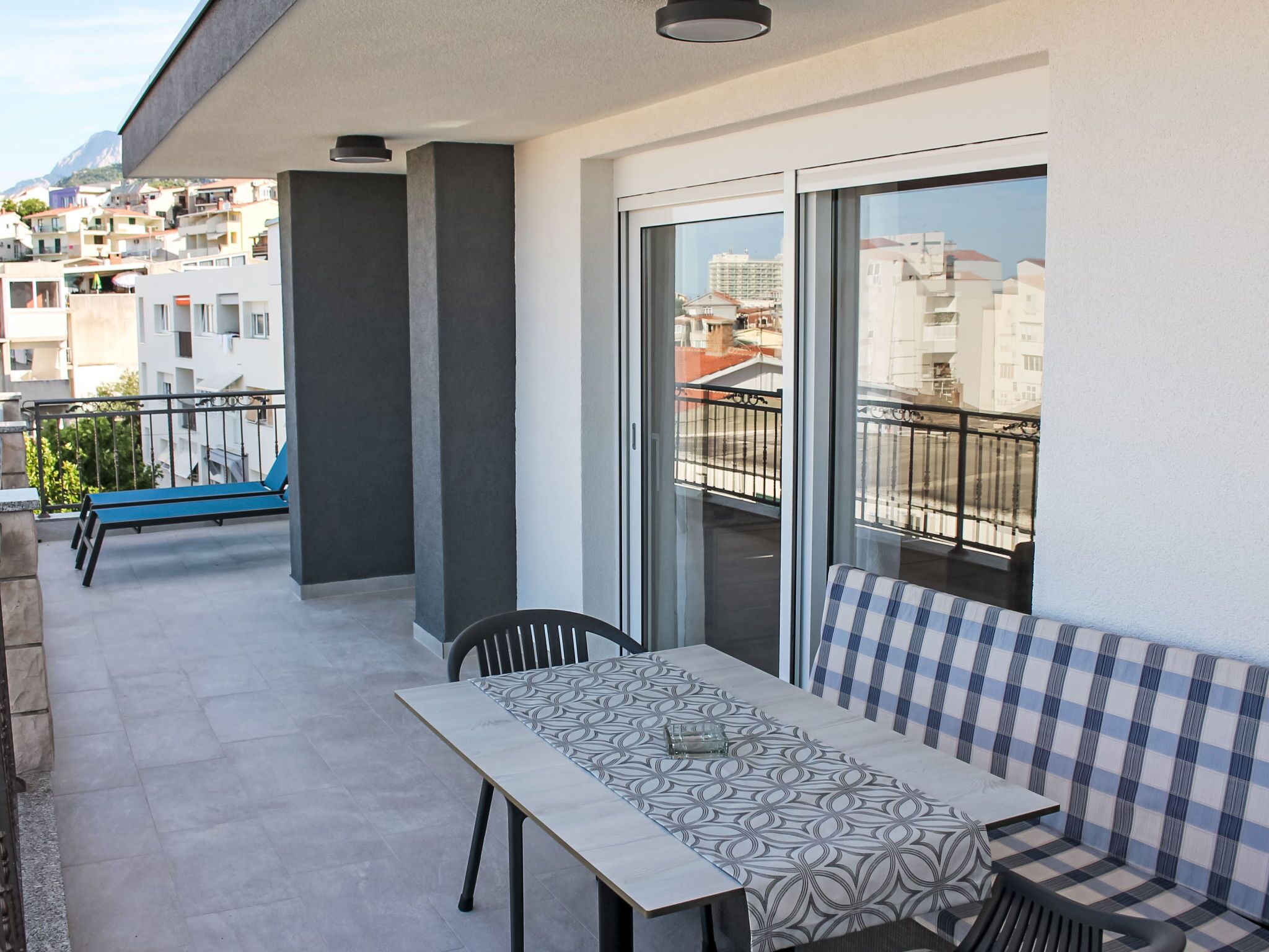 Un balcon avec une table et des chaises, un canapé bleu et une porte vitrée donnant sur une vue de la ville.