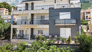 Un immeuble à plusieurs étages doté de balcons, d’une terrasse avec des sièges extérieurs et offrant une vue sur les montagnes en arrière-plan.