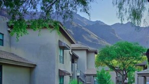 Un edificio residencial con montañas al fondo, un sendero y plantas en macetas.