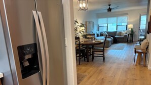 Una cocina moderna con un refrigerador de acero inoxidable, un comedor con una mesa y sillas de madera, y una sala de estar con un sofá y un ventilador de techo.