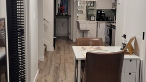 A modern kitchen with white cabinets, a dining area with a table and chairs, and a staircase leading to an upper level. - Your Elegant Escape | Newly Built Prescott Private Suite (Spruce Grove)