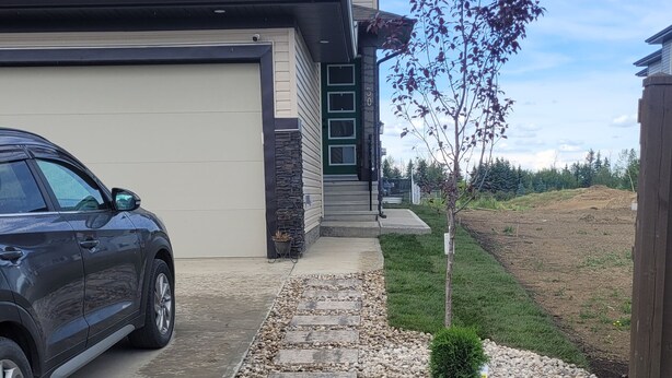 A residential house with a garage, a driveway, and a small garden area with pebbles and a tree. - Your Elegant Escape | Newly Built Prescott Private Suite (Spruce Grove)