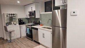 A modern kitchen with stainless steel appliances, a built-in oven, a dishwasher, and a large refrigerator. - Your Elegant Escape | Newly Built Prescott Private Suite (Spruce Grove)