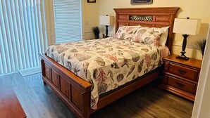 A bedroom with a wooden bed, two bedside tables, a ceiling light, and a window with blinds.