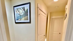 A hallway with wooden flooring, white walls, and a framed picture on the left.