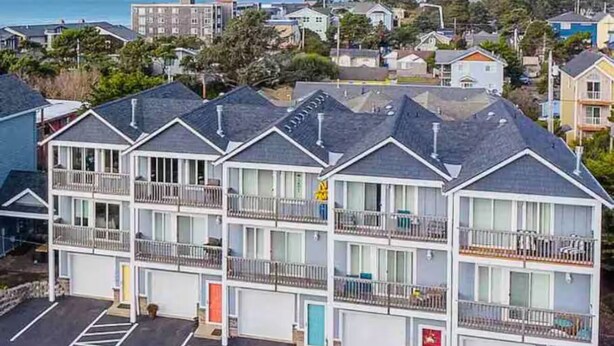 A multi-story motel with a parking lot, balconies, and a view of the ocean.