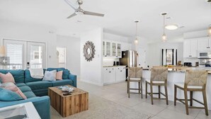 A modern living room with a sofa, coffee table, and a kitchen area with white cabinets and a dining set.