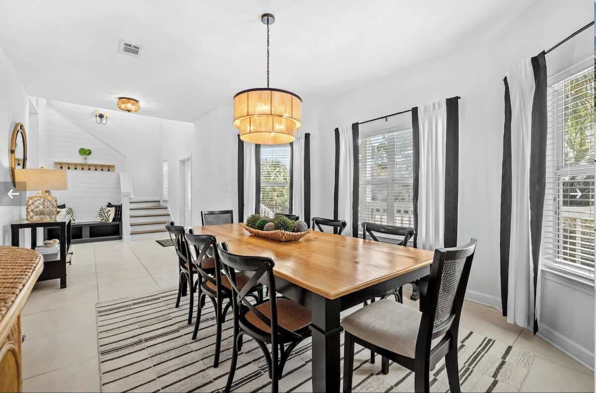 A dining area with a wooden table, black chairs, a hanging light fixture, and a staircase in the background.