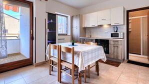 Una cocina compacta con armarios blancos, un microondas y un lavabo. Hay una mesa de comedor con sillas y una ventana con cortinas.