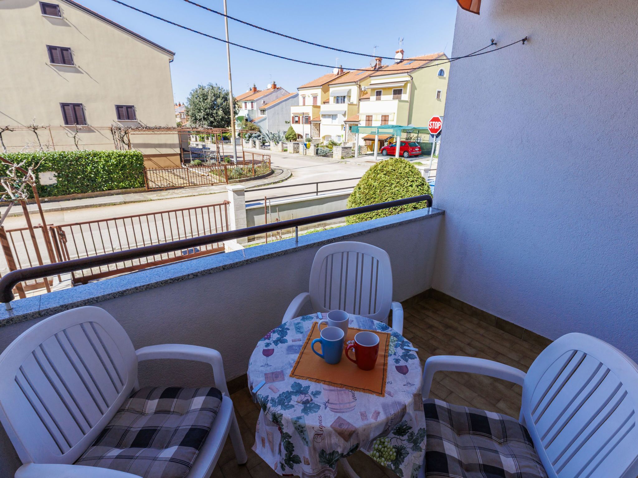 A balcony with two white plastic chairs and a table set with a tablecloth, two cups, and a small orange placemat.