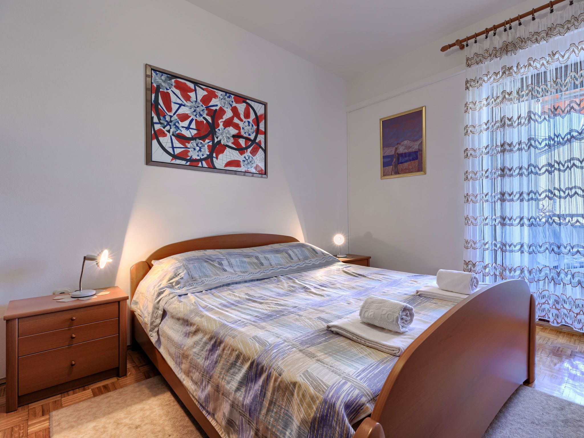 Une chambre à coucher avec un lit, des tables de chevet, une lampe, un tableau et une fenêtre avec des rideaux.