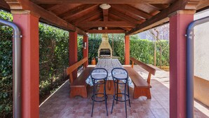 Un patio techado al aire libre con zona de barbacoa, bancos de madera y dos taburetes de bar.