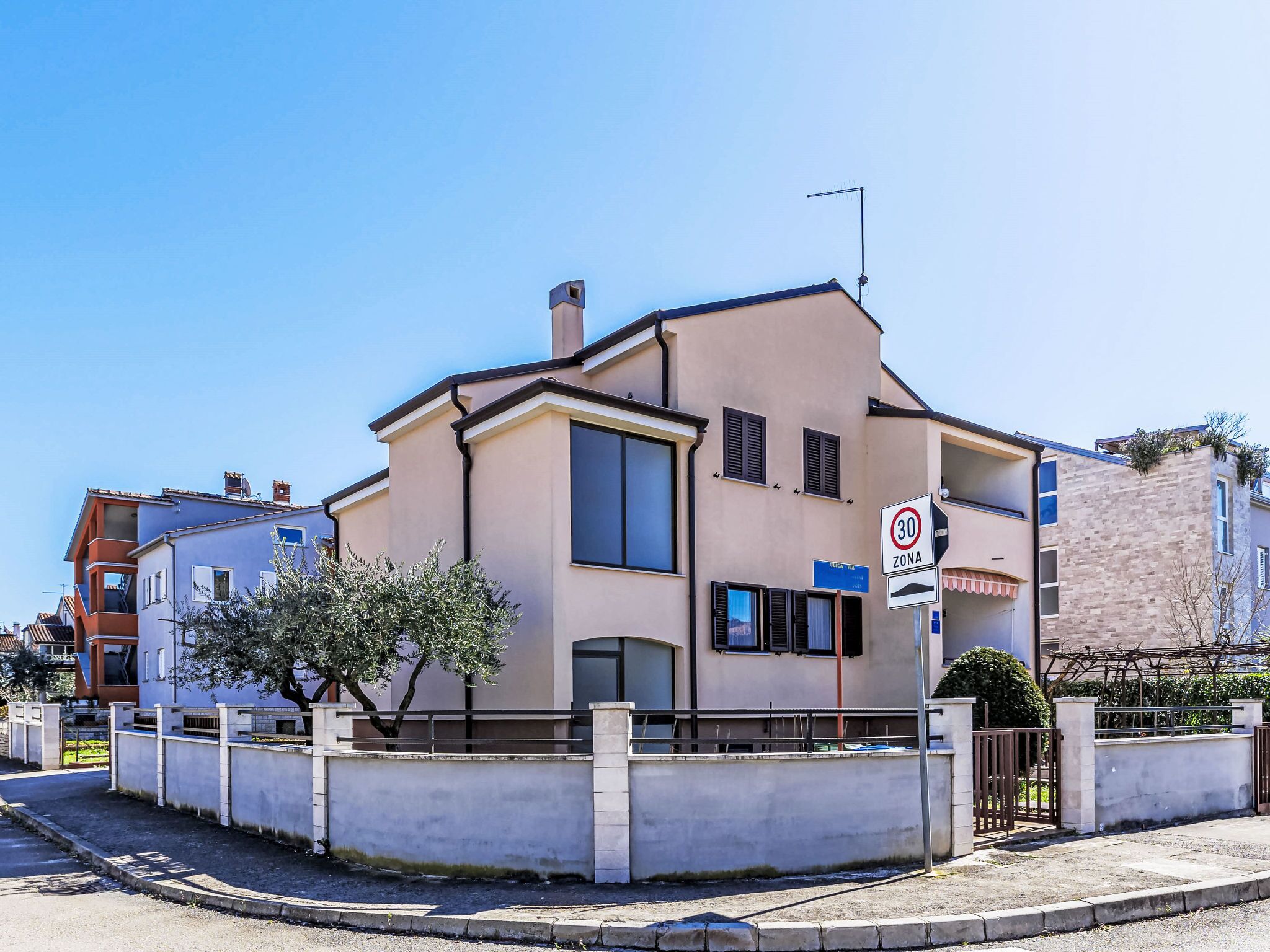 A two-story residential building with a beige facade, large windows, and a visible speed limit sign.