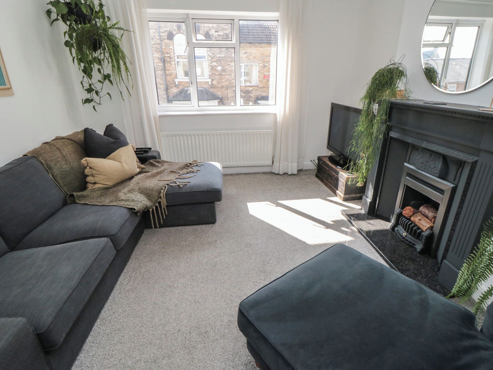A modern living room with a dark grey sofa, a small ottoman, a fireplace, and a television.