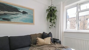 Een moderne woonkamer met een grijze bank, een beige plaid en een hangplant.