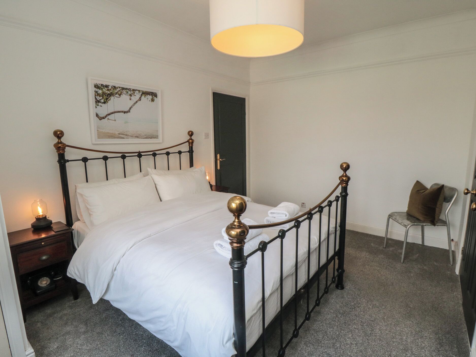 A neatly made bed with white linens, a bedside lamp, and a framed picture on the wall.