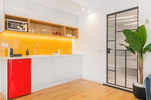 Une cuisine moderne avec des meubles blancs, un réfrigérateur rouge et une étagère en bois où sont rangés les ustensiles de cuisine.