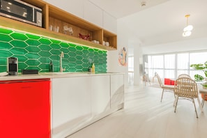 Una cocina moderna con un electrodoméstico rojo, armarios blancos y un salpicadero verde.
