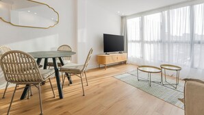 A modern living room with a dining table, chairs, a TV, and a large window with sheer curtains. - Ototo Luxury Living (Thessaloniki)