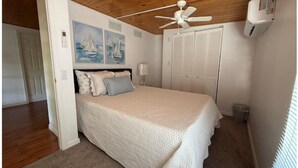 A bedroom with a bed, a ceiling fan, a wall-mounted air conditioner, and a door leading to another room. - The Bamboo house on the lake (Hernando)