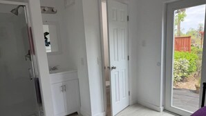A bathroom with a shower, a sink, and a door leading to a patio. - The workshop room @ Bamboo house (Hernando)