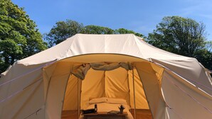 A large, beige tent with a bed inside, surrounded by trees.